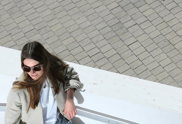 Britta Reineke leaning on a white wall in front of a gray IONIQ 5. She has long brunette hair and is wearing large tortoise shell sunglasses and a beige jacket.